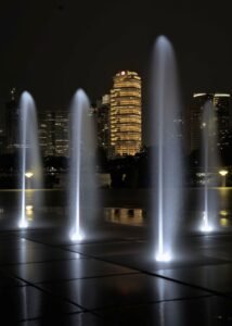 City skyline with illuminated fountains at night, showcasing urban architecture.